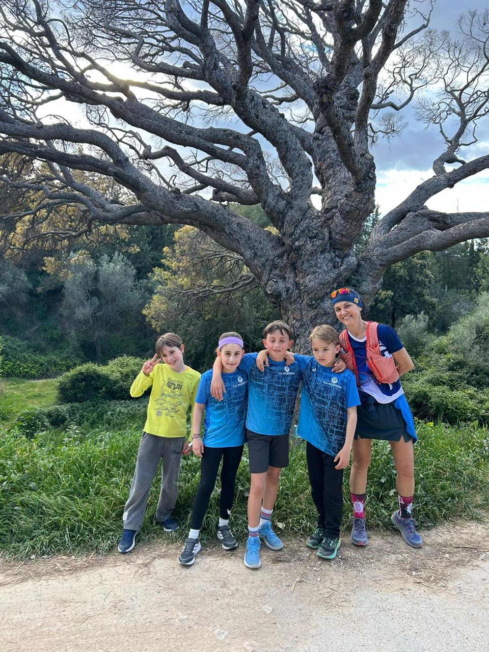 Grup de joves i una persona adulta al costat d’un arbre, en un camí.