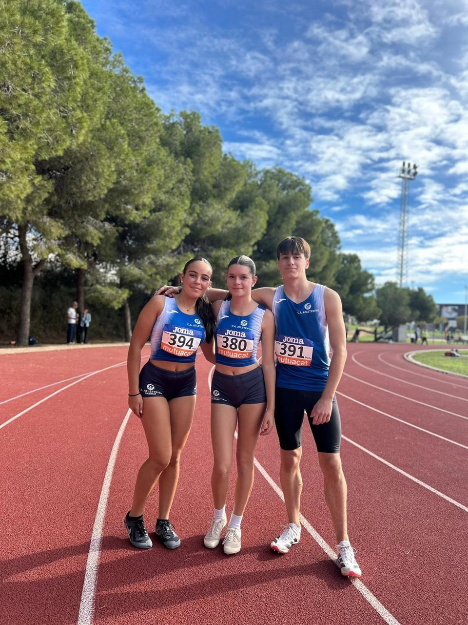Tres joves amb roba esportiva posant a la pista.